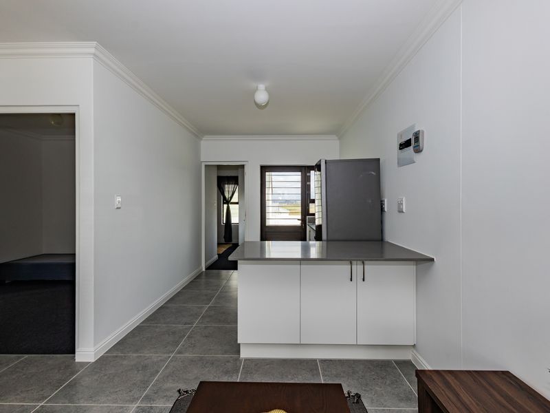 A clean, modern kitchen area featuring white cabinetry, stone countertops, and neutral tiled flooring, providing a functional and well-maintained space.
