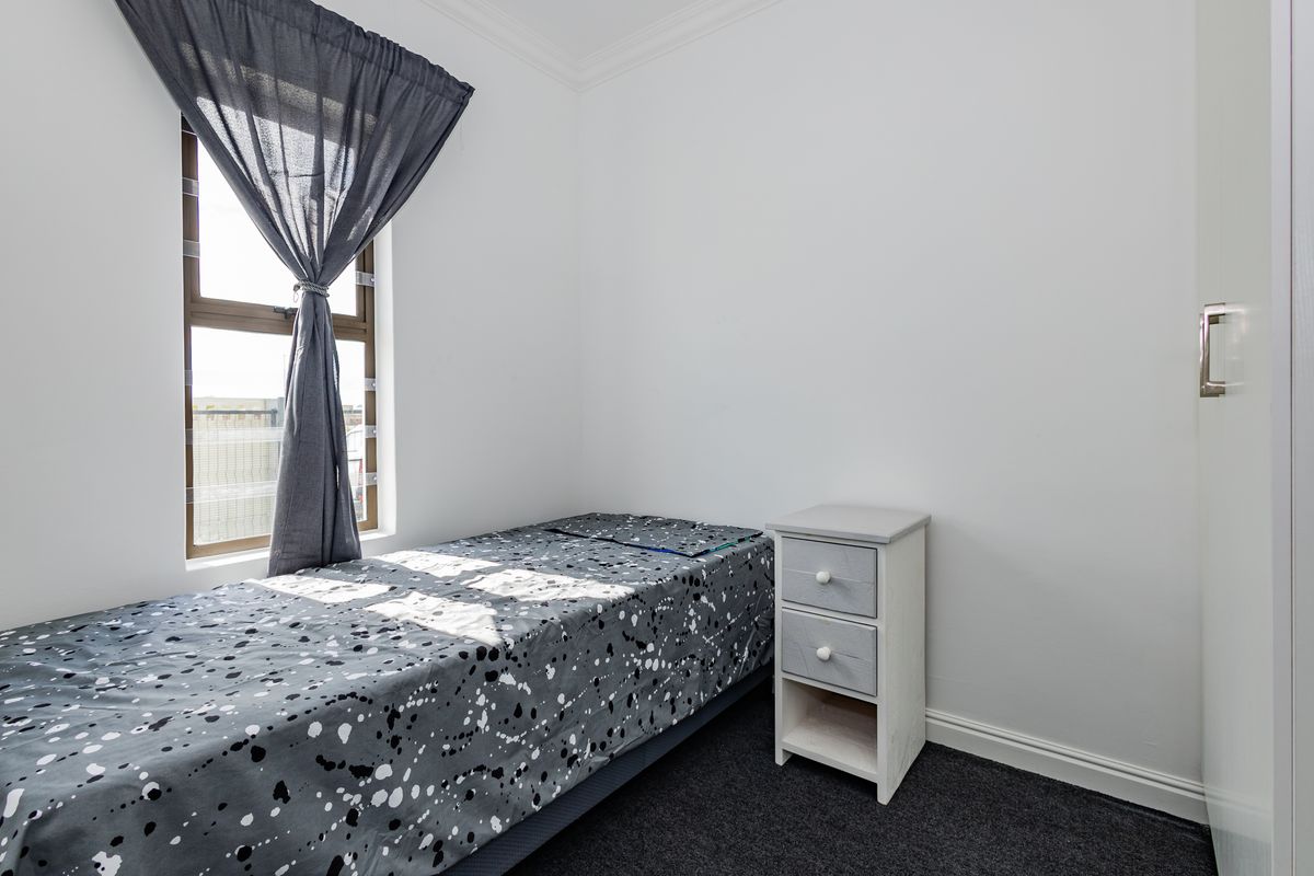 A clean, neutral bedroom featuring a built-in wardrobe, dark carpeting, and a window with natural light.