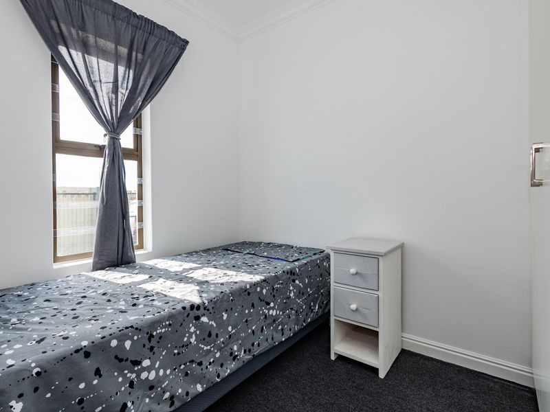 A clean, neutral bedroom featuring a built-in wardrobe, dark carpeting, and a window with natural light.