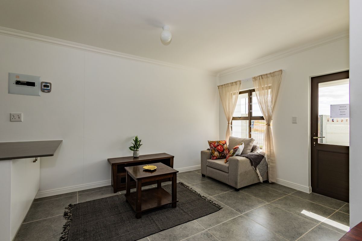 A bright living area featuring neutral tiled flooring, crisp white walls, and direct access to the exterior via a solid door.