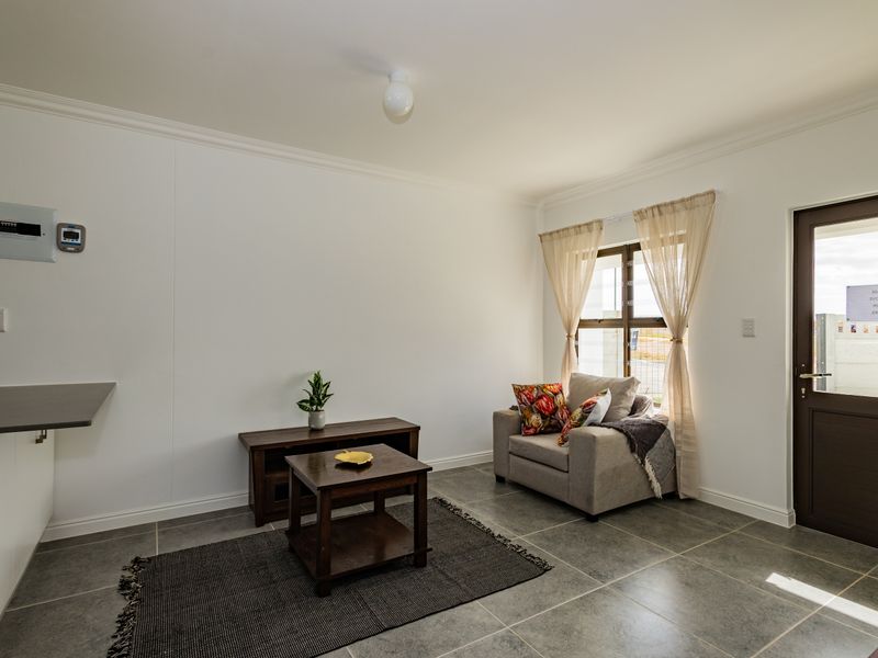 A bright living area featuring neutral tiled flooring, crisp white walls, and direct access to the exterior via a solid door.