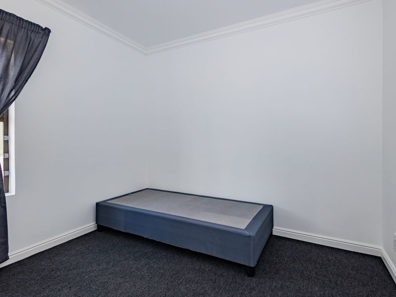 A clean, neutral bedroom featuring dark carpeting, white walls, and decorative cornice detailing, providing a blank canvas for personalization.