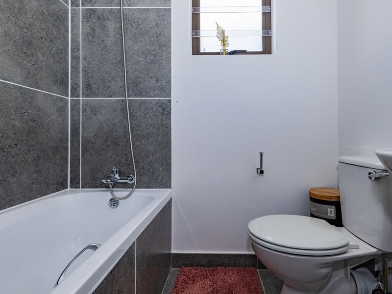 A clean, modern bathroom featuring a bathtub with shower mixer, pedestal basin, and toilet, finished with contemporary grey wall tiles.