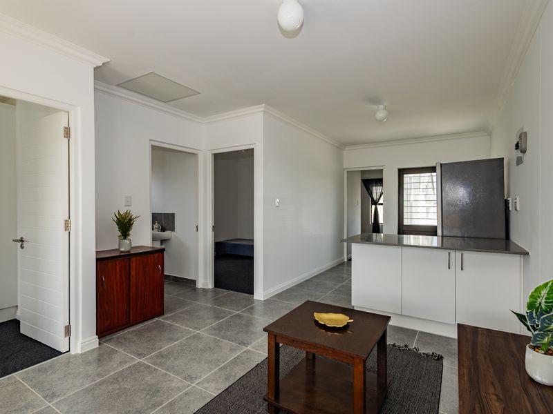 Open plan living area featuring tiled flooring, neutral walls, and a compact kitchen with modern cabinetry and stone countertops.