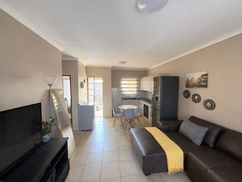 Open-plan living area featuring tiled flooring, a functional kitchen with built-in cabinetry and appliances, and direct access to an outdoor balcony.