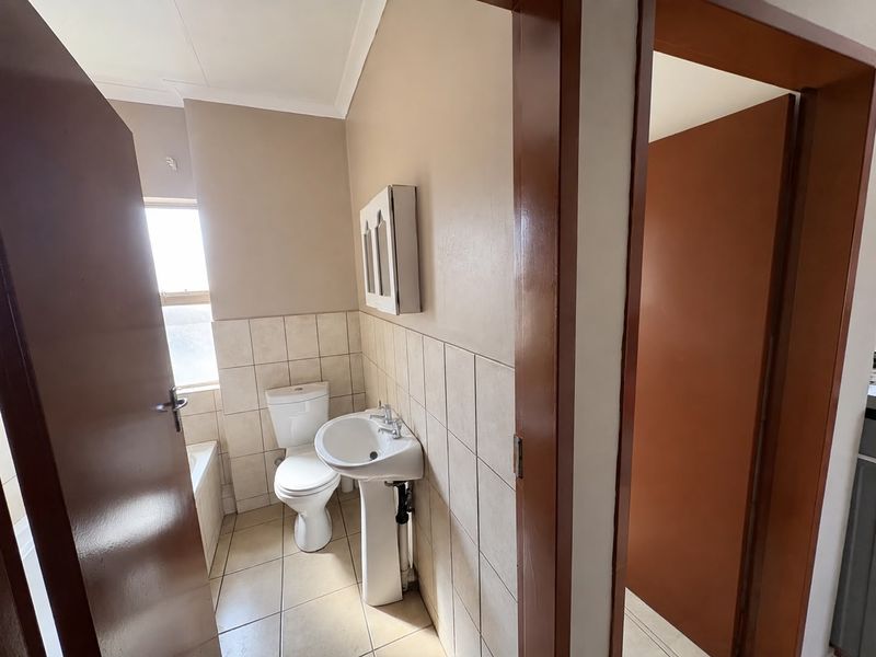 A functional bathroom featuring a pedestal basin, toilet, and bathtub with neutral wall and floor tiling.