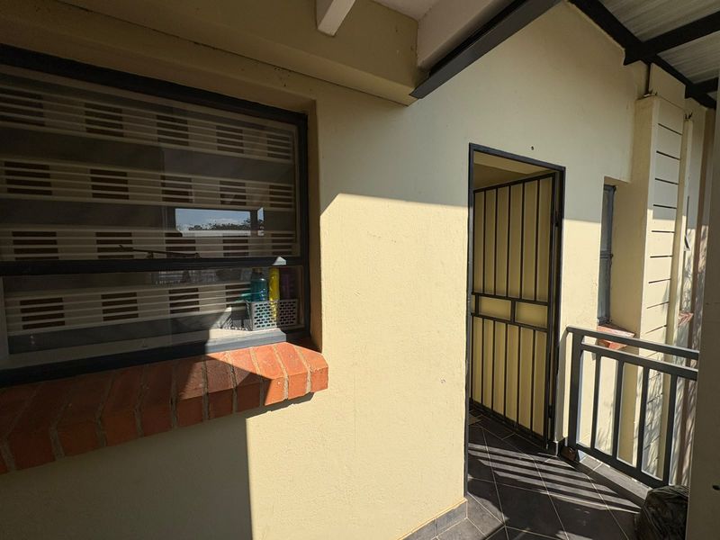 A covered balcony area featuring tiled flooring, a brick window sill, and a secure metal entrance gate.