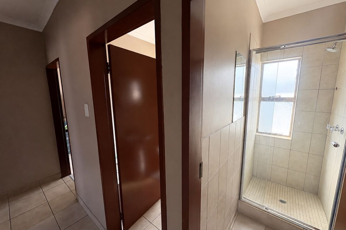 A functional bathroom featuring a glass-enclosed shower, neutral wall and floor tiling, and multiple internal doorways leading to adjacent rooms.
