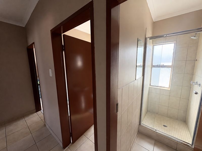 A functional bathroom featuring a glass-enclosed shower, neutral wall and floor tiling, and multiple internal doorways leading to adjacent rooms.
