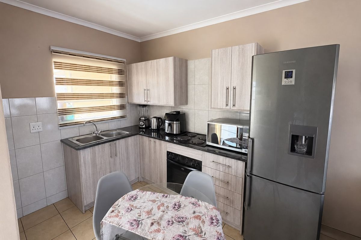 A functional kitchen featuring light wood-grain cabinetry, granite countertops, a built-in oven, electric hob, and tiled finishes throughout.