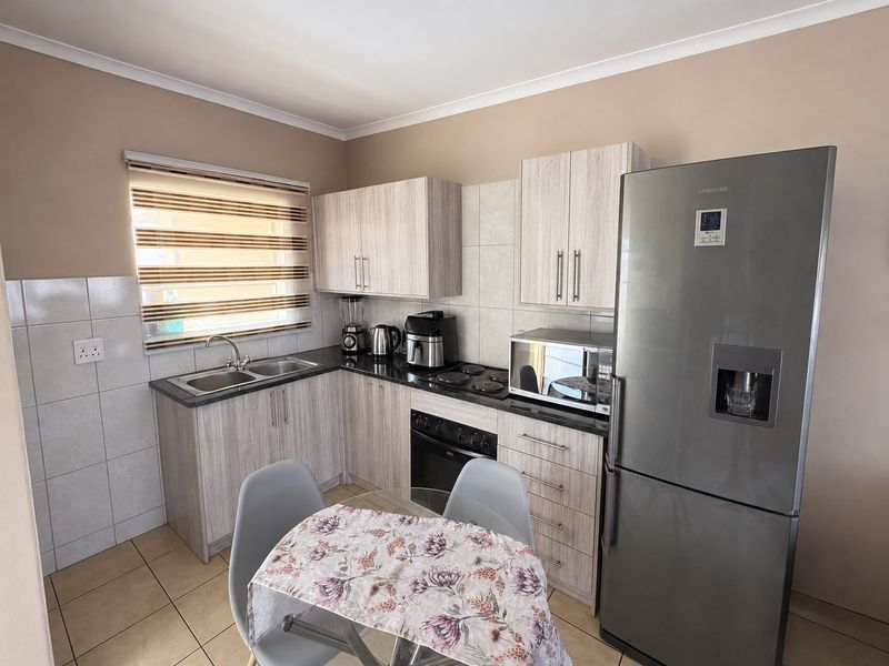 A functional kitchen featuring light wood-grain cabinetry, granite countertops, a built-in oven, electric hob, and tiled finishes throughout.