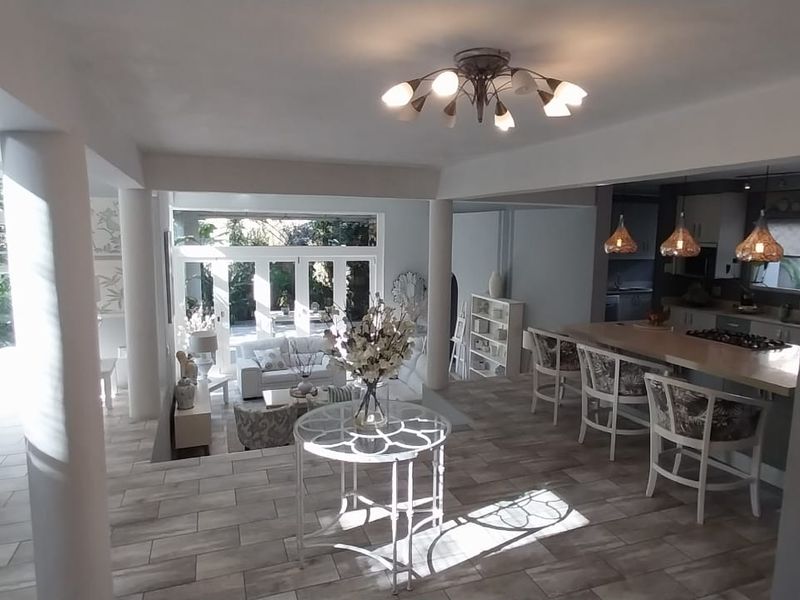 Spacious open-plan living area featuring tiled floors, a central kitchen island with hob, and seamless flow to the outdoor patio through french doors.