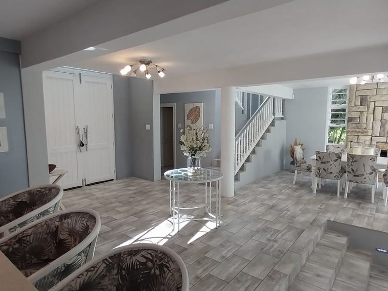 Spacious open-plan living and dining area featuring modern tiled flooring, a stone feature wall, and an elegant staircase.