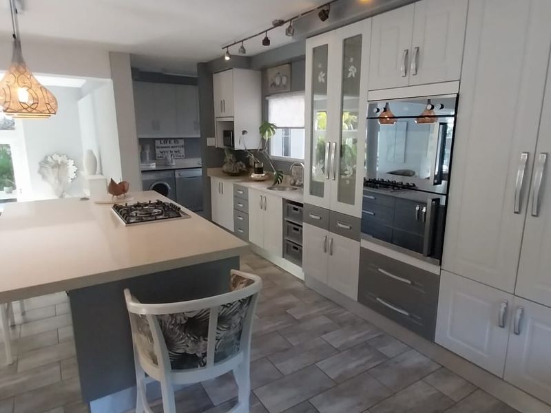Modern kitchen featuring a central island with a gas hob, integrated cabinetry, built-in oven, and tiled flooring, offering a functional and well-maintained cooking space.