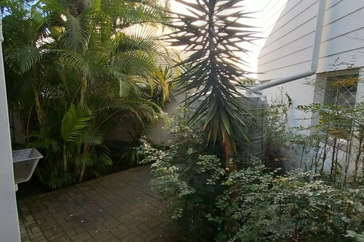 A private rear courtyard featuring paved flooring, a water tank, and a utility sink, surrounded by established garden greenery.