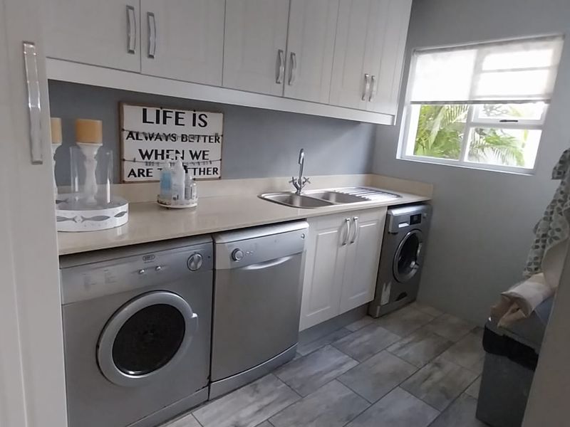 A functional laundry room featuring built-in white cabinetry, a stainless steel sink, and modern tiled flooring with space for multiple appliances.