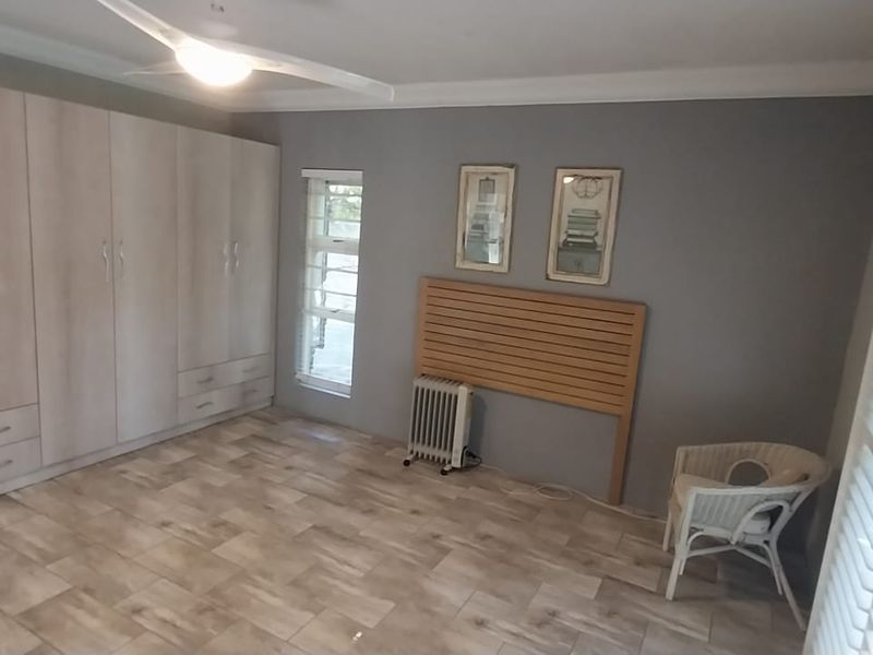 Spacious bedroom featuring extensive built-in cabinetry, tiled flooring, ceiling fan, and plantation shutters, offering a clean and well-maintained living space.