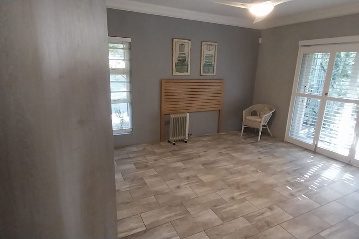 A spacious bedroom featuring neutral tiled flooring, crown molding, and large sliding glass doors with plantation shutters providing ample natural light.