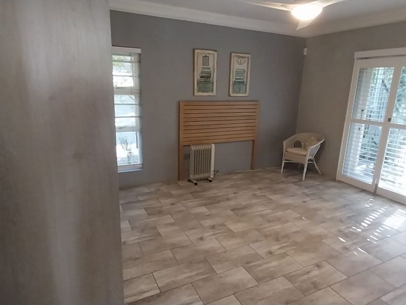 A spacious bedroom featuring neutral tiled flooring, crown molding, and large sliding glass doors with plantation shutters providing ample natural light.