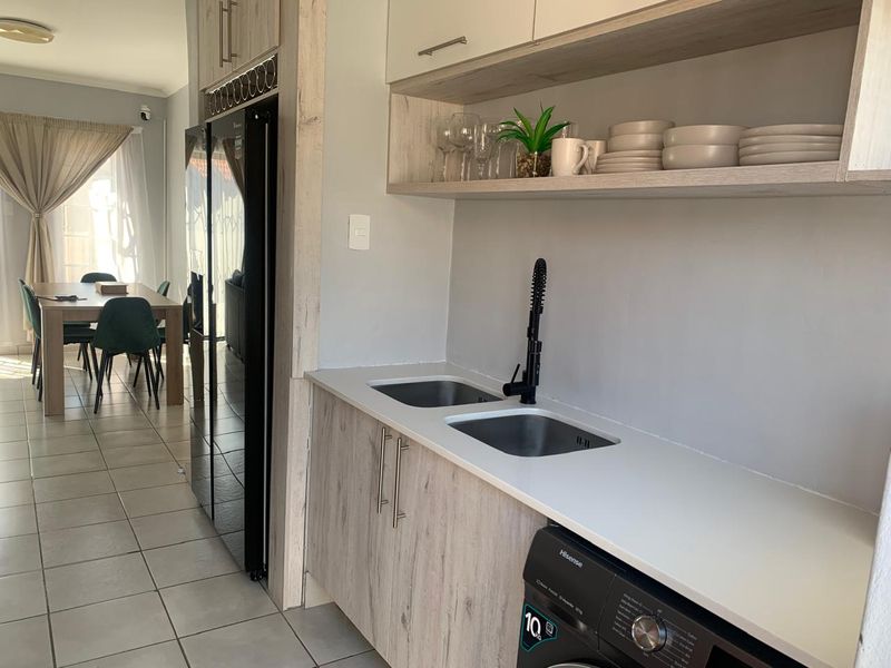A modern scullery area featuring built-in cabinetry, double stainless steel sink with a black mixer tap, and open shelving, adjacent to the dining space.