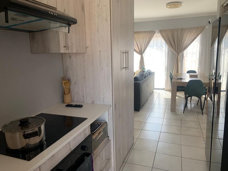 Open-plan kitchen and dining area featuring modern light wood cabinetry, integrated appliances, and tiled flooring leading to a bright living space.