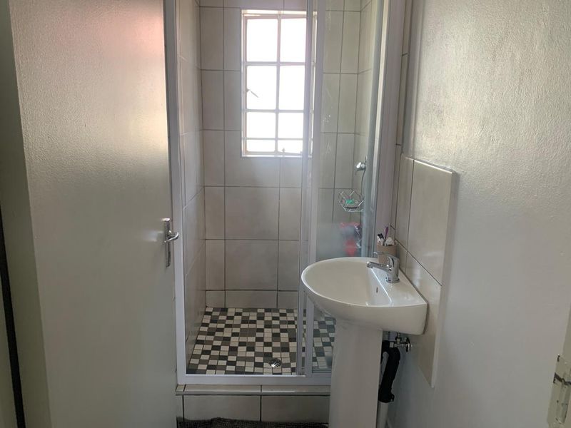 A compact bathroom featuring a pedestal basin and a separate shower enclosure with tiled finishes.