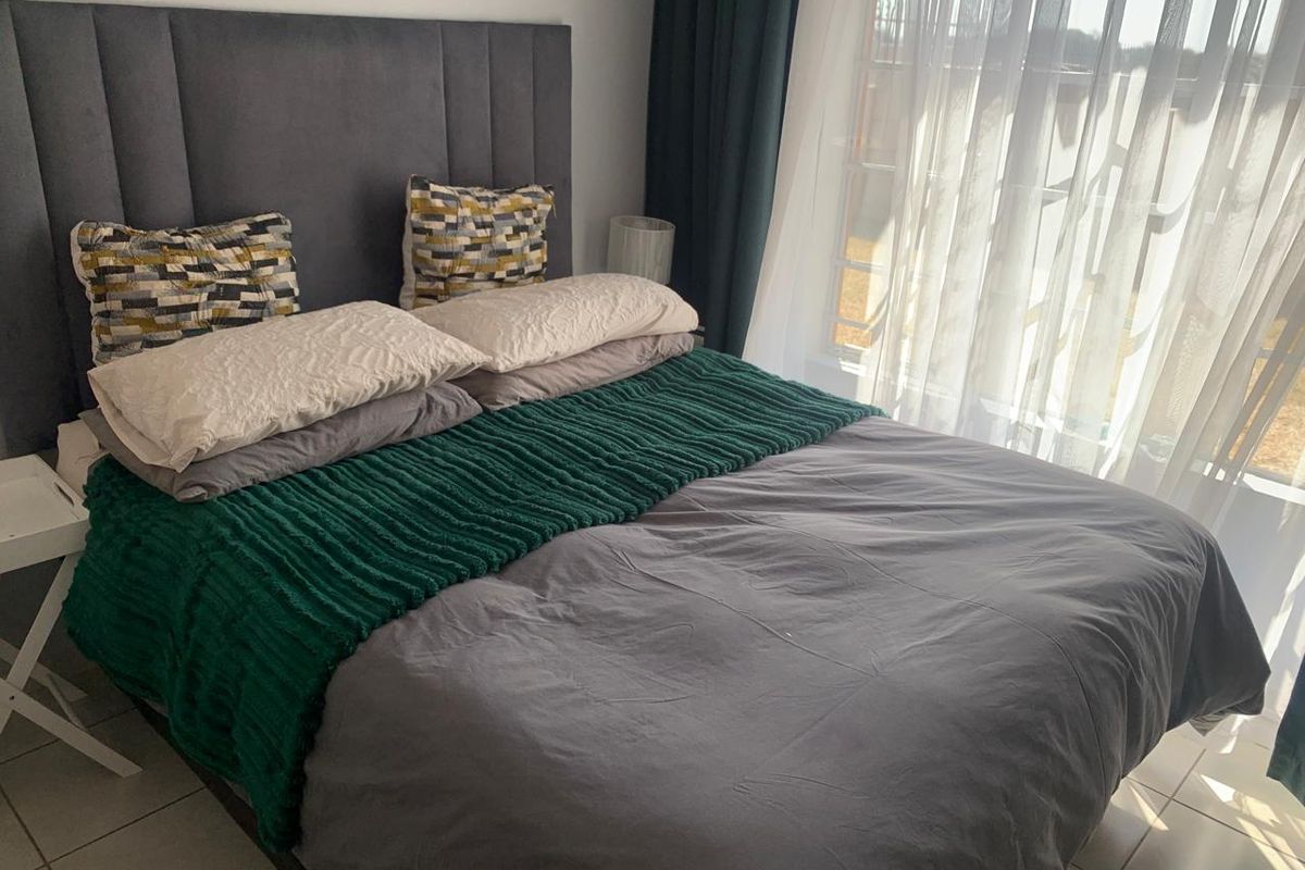 A well-lit bedroom featuring tiled flooring and large windows with installed curtain tracks.