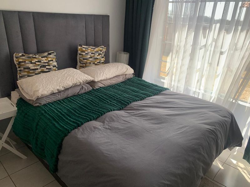 A well-lit bedroom featuring tiled flooring and large windows with installed curtain tracks.