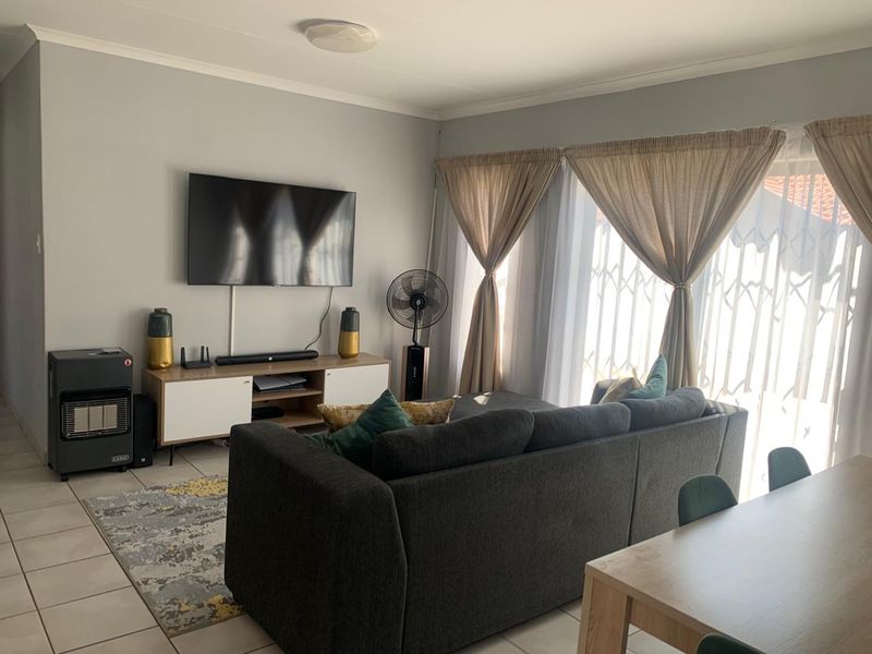 An open-plan living area featuring tiled flooring and a sliding door with security gate, providing access to the exterior.