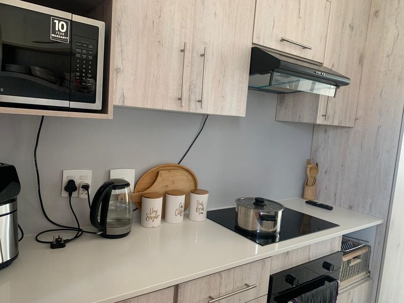 Modern kitchen featuring light wood-grain cabinetry, white quartz countertops, a built-in oven, electric hob, and integrated extractor fan.