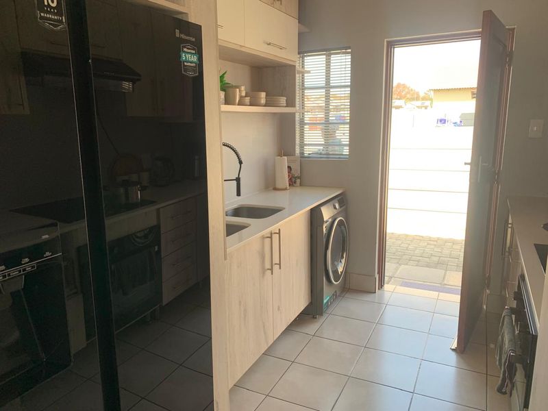 A functional scullery featuring modern light wood cabinetry, a double sink, built-in oven, and direct access to the exterior.
