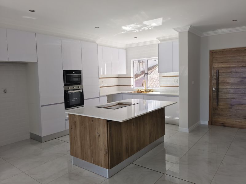 Modern kitchen featuring white glossy cabinetry, a central island with stone countertops, built-in oven and microwave, and elegant brass fixtures.