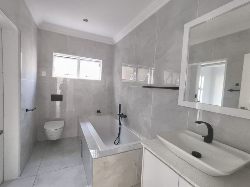 Modern bathroom featuring a built-in bathtub, wall-mounted toilet, vessel sink with black fixtures, and neutral floor-to-ceiling tiling.