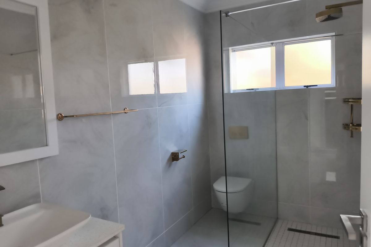 Modern bathroom featuring a walk-in shower with glass screen, wall-mounted toilet, and contemporary vanity basin with marble-look wall tiling.