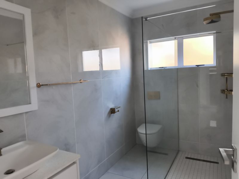 Modern bathroom featuring a walk-in shower with glass screen, wall-mounted toilet, and contemporary vanity basin with marble-look wall tiling.