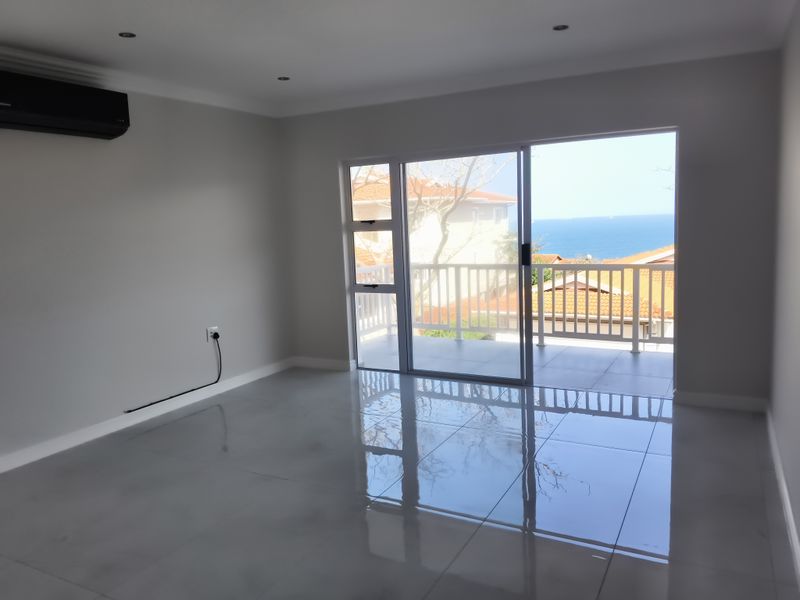 Bright and spacious living area featuring polished tiled floors, air conditioning, and direct access to a balcony with scenic ocean views.