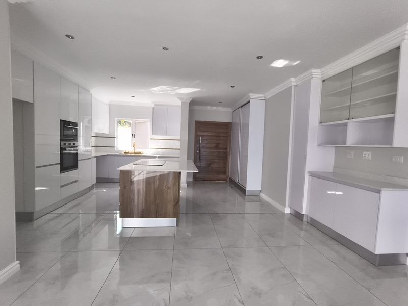 Modern, spacious kitchen featuring high-gloss cabinetry, a central island, built-in appliances, and sleek tiled flooring in an open-plan layout.