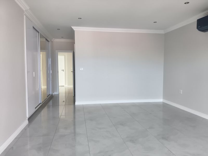 A spacious, modern bedroom featuring polished porcelain floor tiles, built-in cupboards with sliding mirror doors, recessed lighting, and a wall-mounted air conditioning unit.