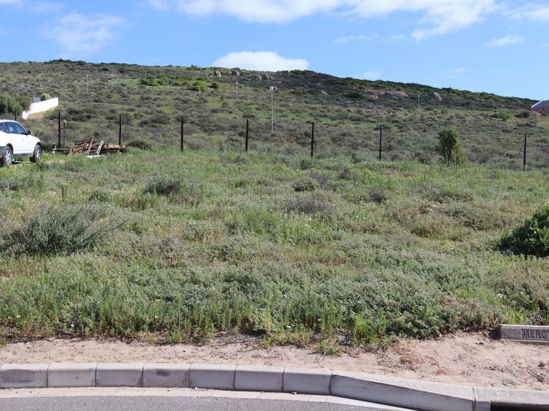 A vacant residential plot featuring natural vegetation, perimeter fencing, and street-level curb access, situated in a hillside neighborhood.