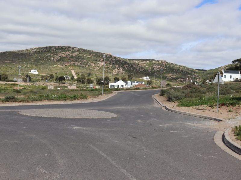 A view of the paved street and roundabout infrastructure within the residential estate, featuring surrounding natural landscape and hillside views.