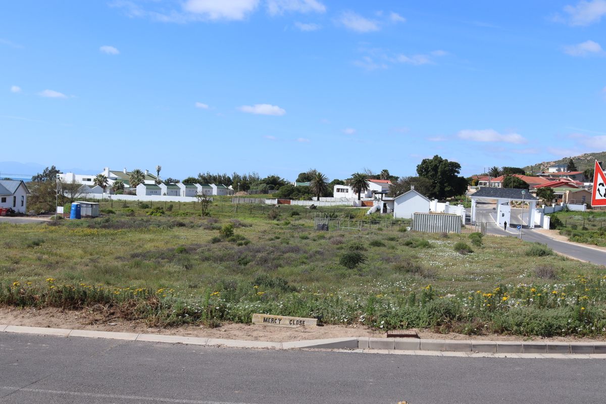 A vacant residential plot of land located on a corner, featuring natural vegetation and direct access to a paved street.