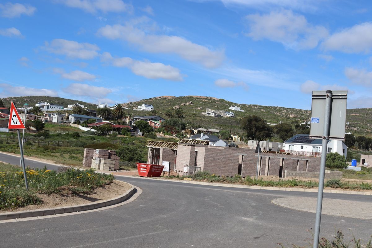 A view of a residential property under construction, featuring exposed masonry walls and timber roof framing in a developing coastal neighborhood.