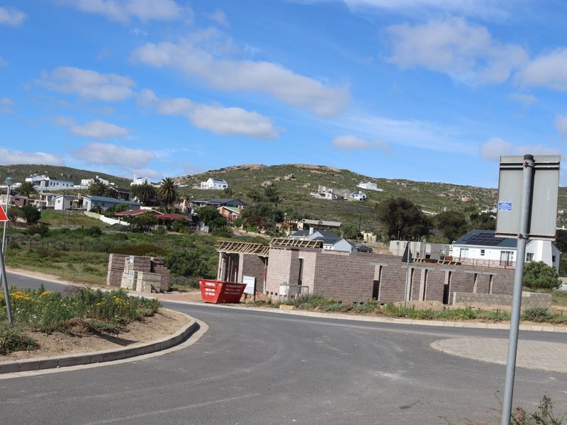 A view of a residential property under construction, featuring exposed masonry walls and timber roof framing in a developing coastal neighborhood.