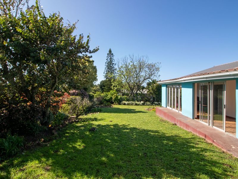 A spacious rear garden featuring a well-maintained lawn, mature trees, and a concrete patio area accessible through large sliding glass doors.
