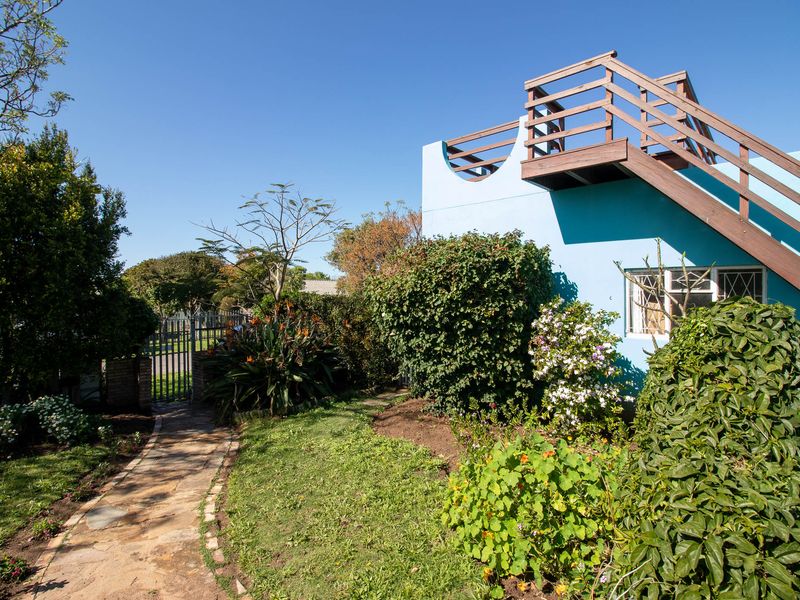 Rear garden view featuring a stone pathway, established landscaping, and an external wooden staircase leading to an upper balcony area.