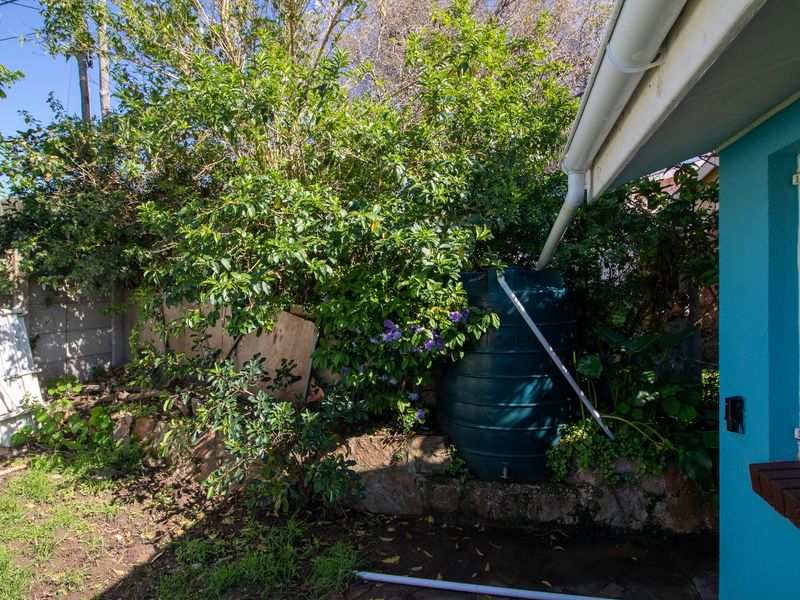 Rear garden area featuring a water tank, stone retaining wall, and guttering system along the side of the house.