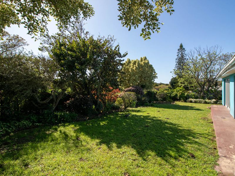 A spacious rear garden featuring a lawn area, mature trees, and a concrete patio adjacent to the house with sliding door access.