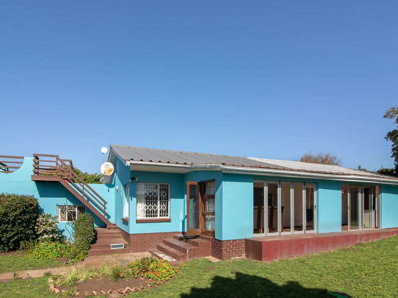 Rear view of a single-story house featuring a metal roof, folding glass doors, and an external staircase leading to a rooftop terrace area.