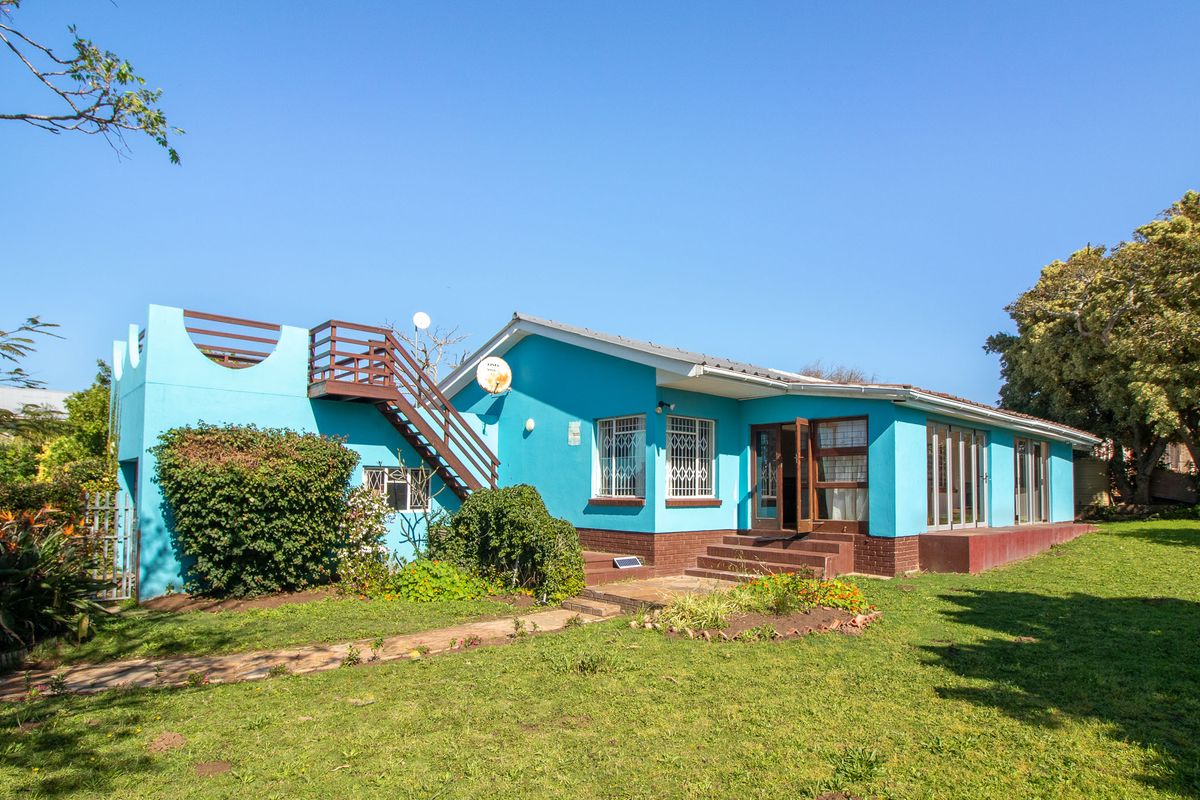 Rear view of a blue house featuring an external staircase leading to a roof terrace, set within a spacious garden area.