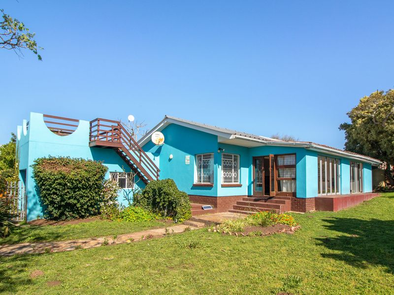 Rear view of a blue house featuring an external staircase leading to a roof terrace, set within a spacious garden area.
